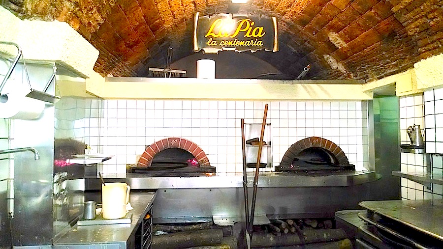 La Pia, in the center of La Spezia, Italy. Wood is stacked below the ovens, and deep in the left oven, a farinata is cooking.