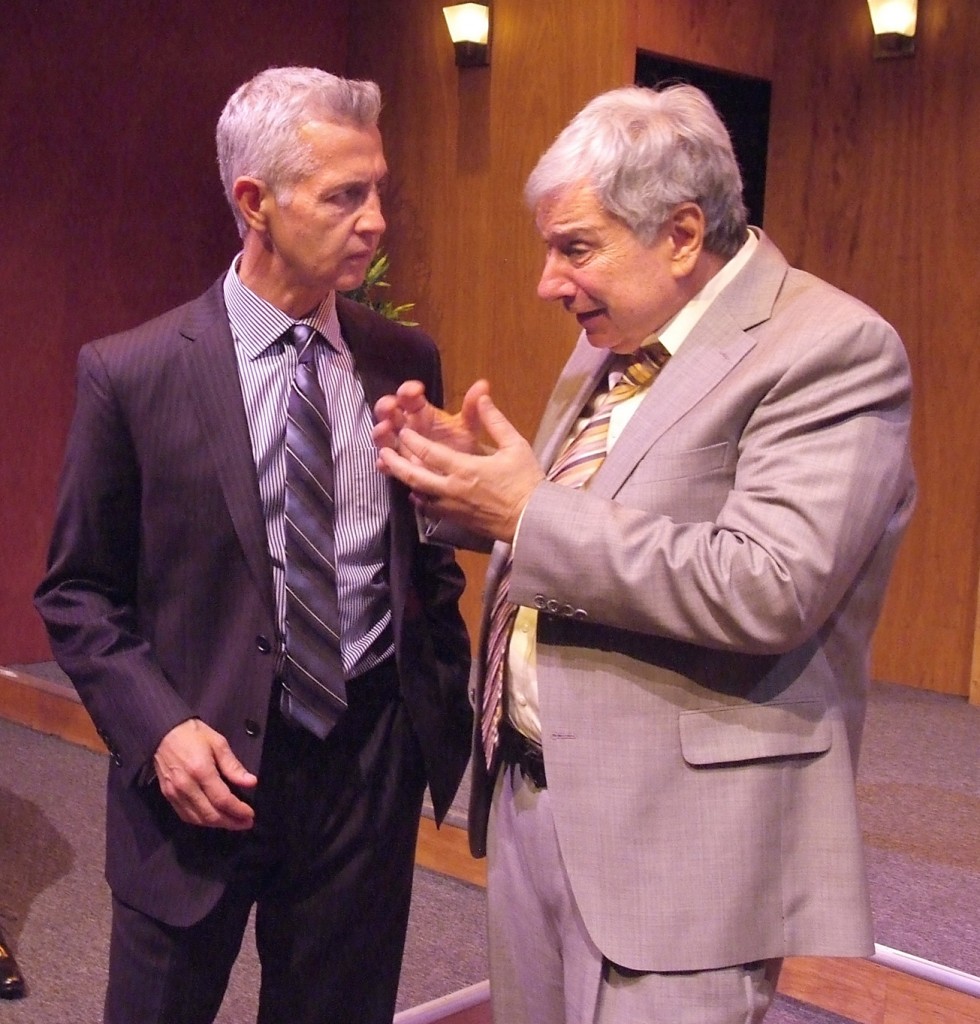 two men in suits, one light, one dark, gray hair, in intense conversation