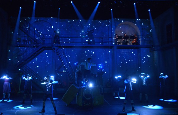 blue lit stage with a group of people each holding white lights